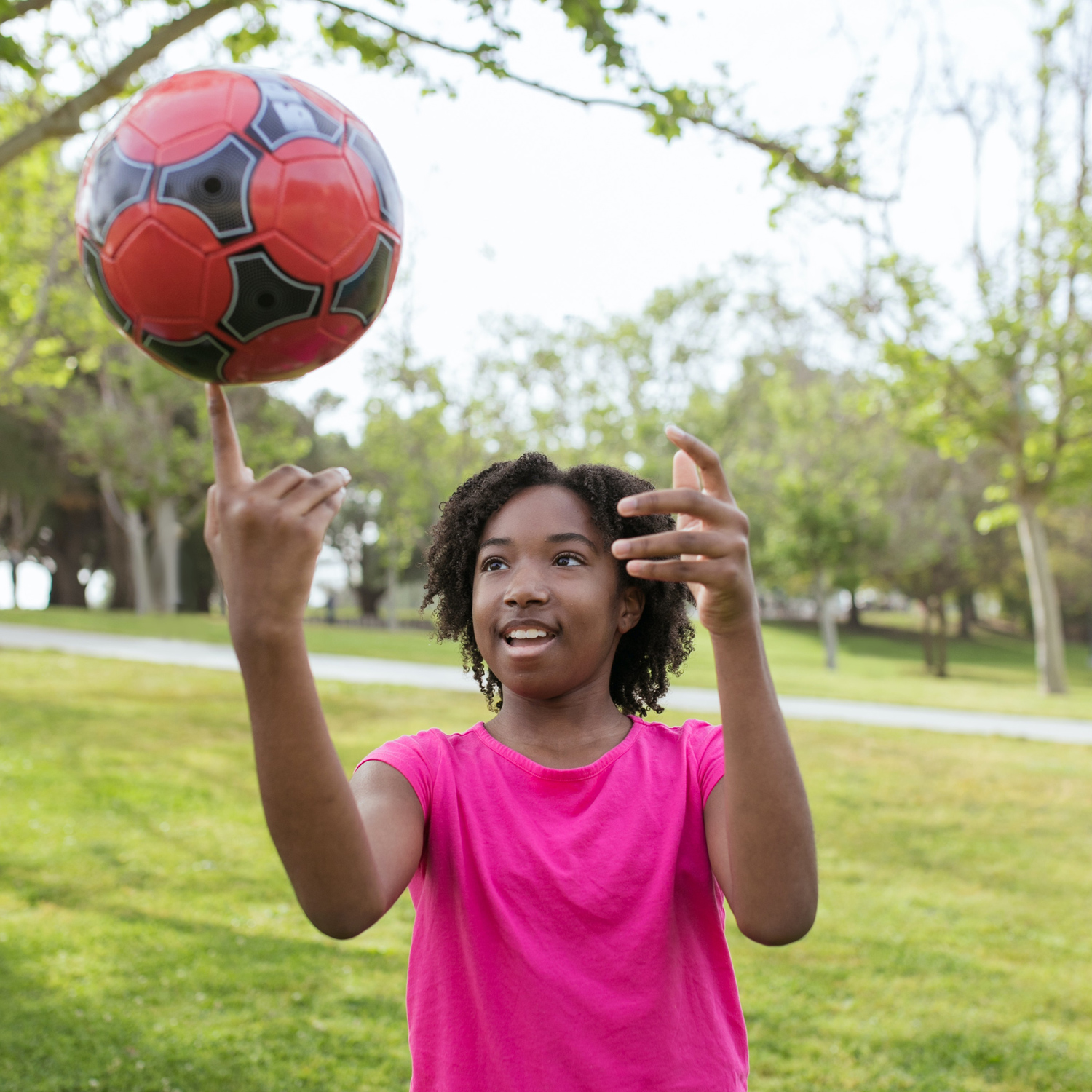 A young girl wearing a pink top spins a ball on her finger in the park